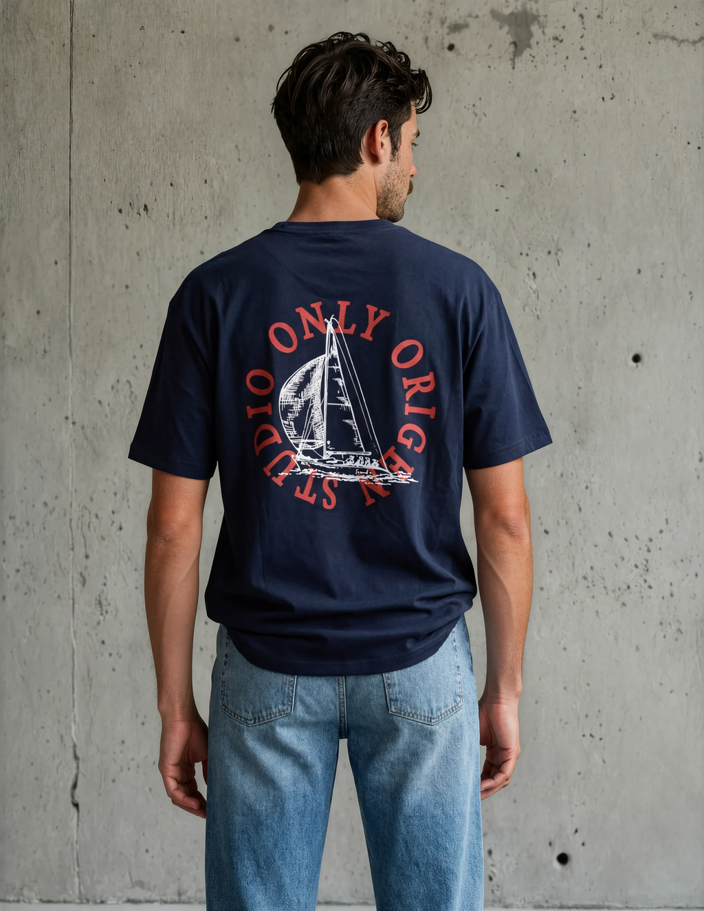 Vista de espalda completa de modelo masculino con camiseta azul marino de algodón; destaca un gran gráfico circular rojo con la ilustración de un velero y el texto "Only Origen Studio".
