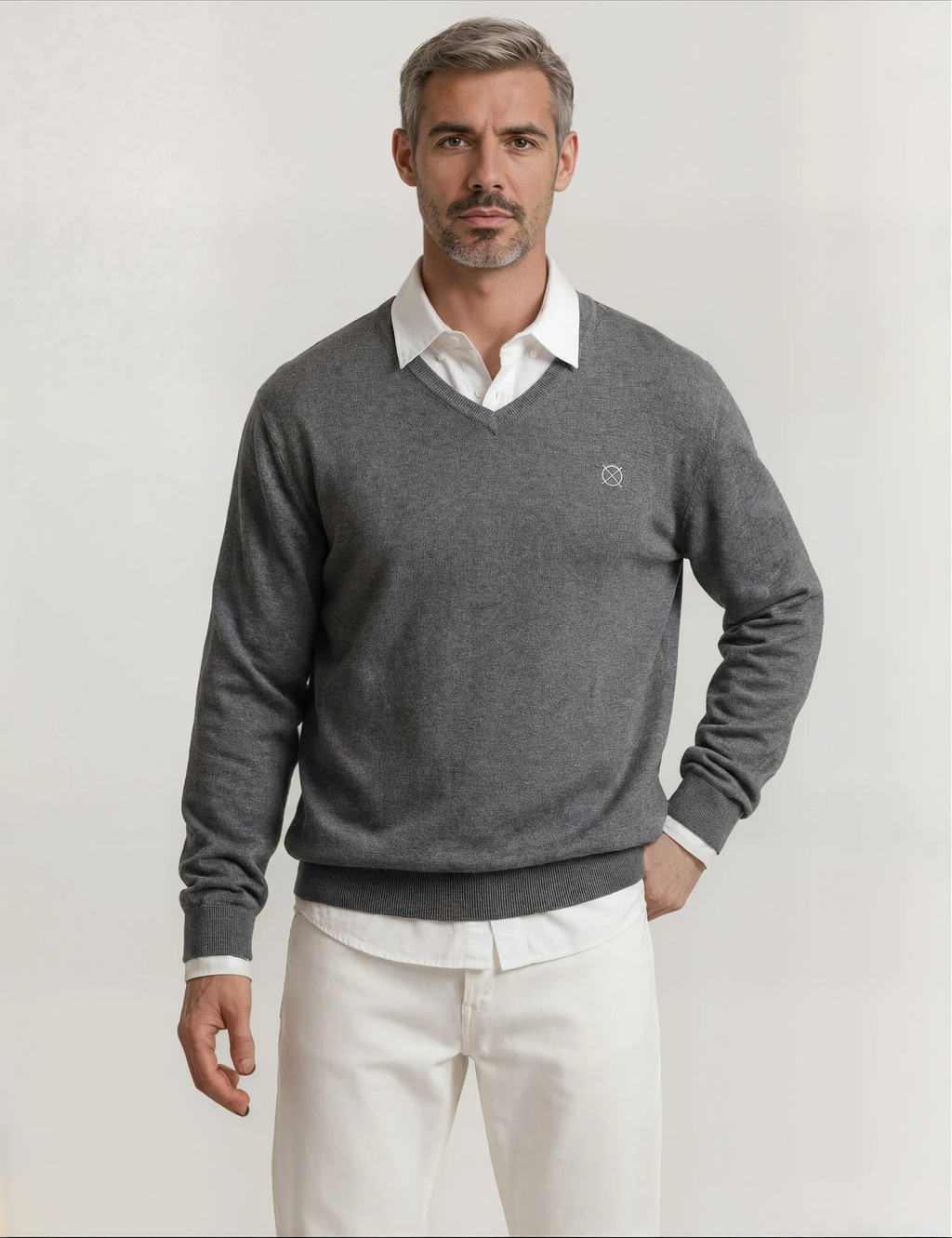 Jersey gris de hombre Origen Studio con cuello pico y logo bordado, combinado con camisa blanca y pantalón claro.