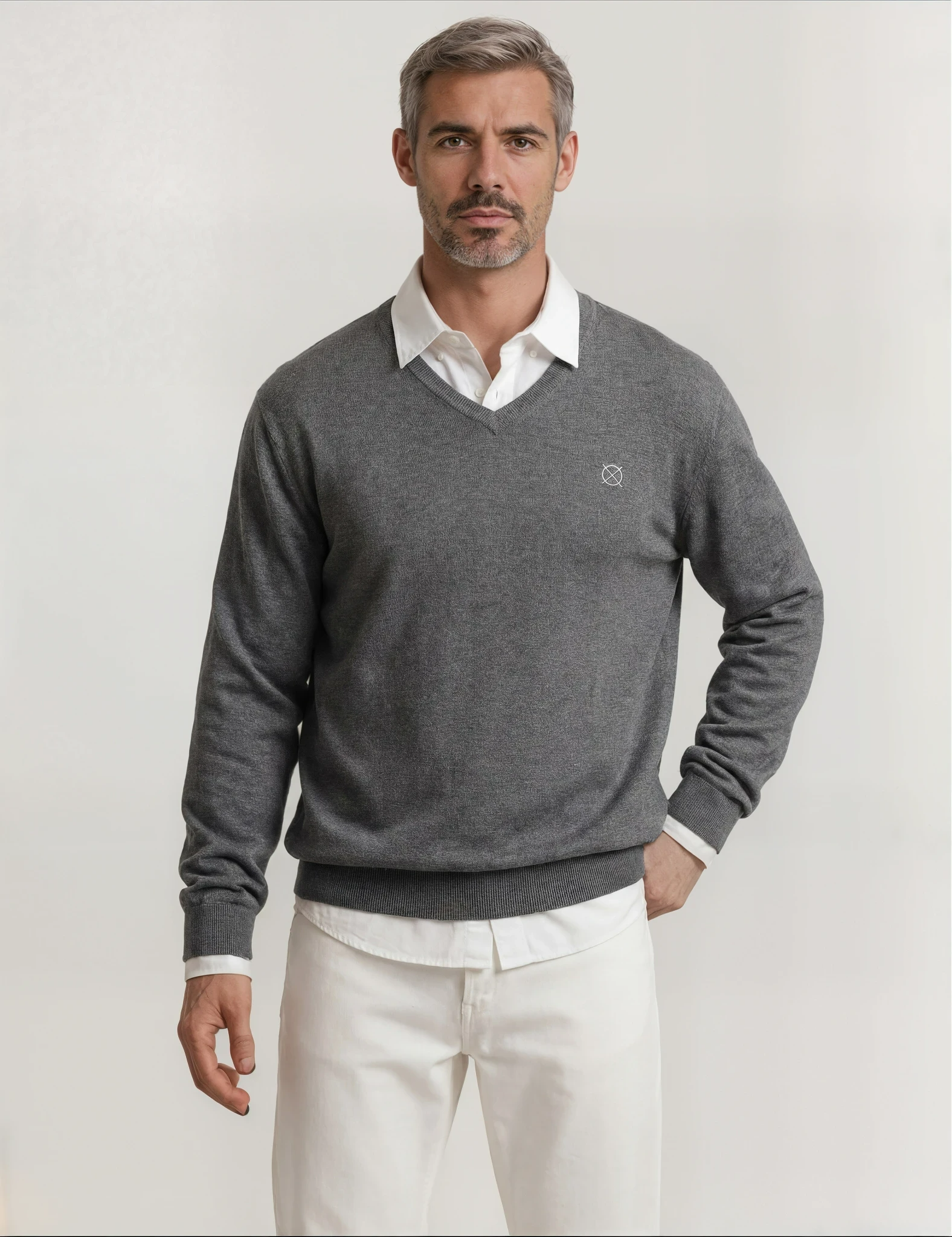 Jersey gris de hombre Origen Studio con cuello pico y logo bordado, combinado con camisa blanca y pantalón claro.
