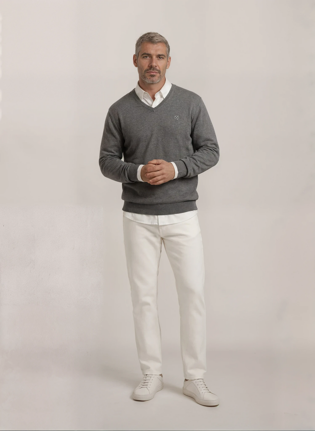 Look completo con jersey gris cuello pico Origen Studio para hombre combinado con pantalón blanco y zapatillas.