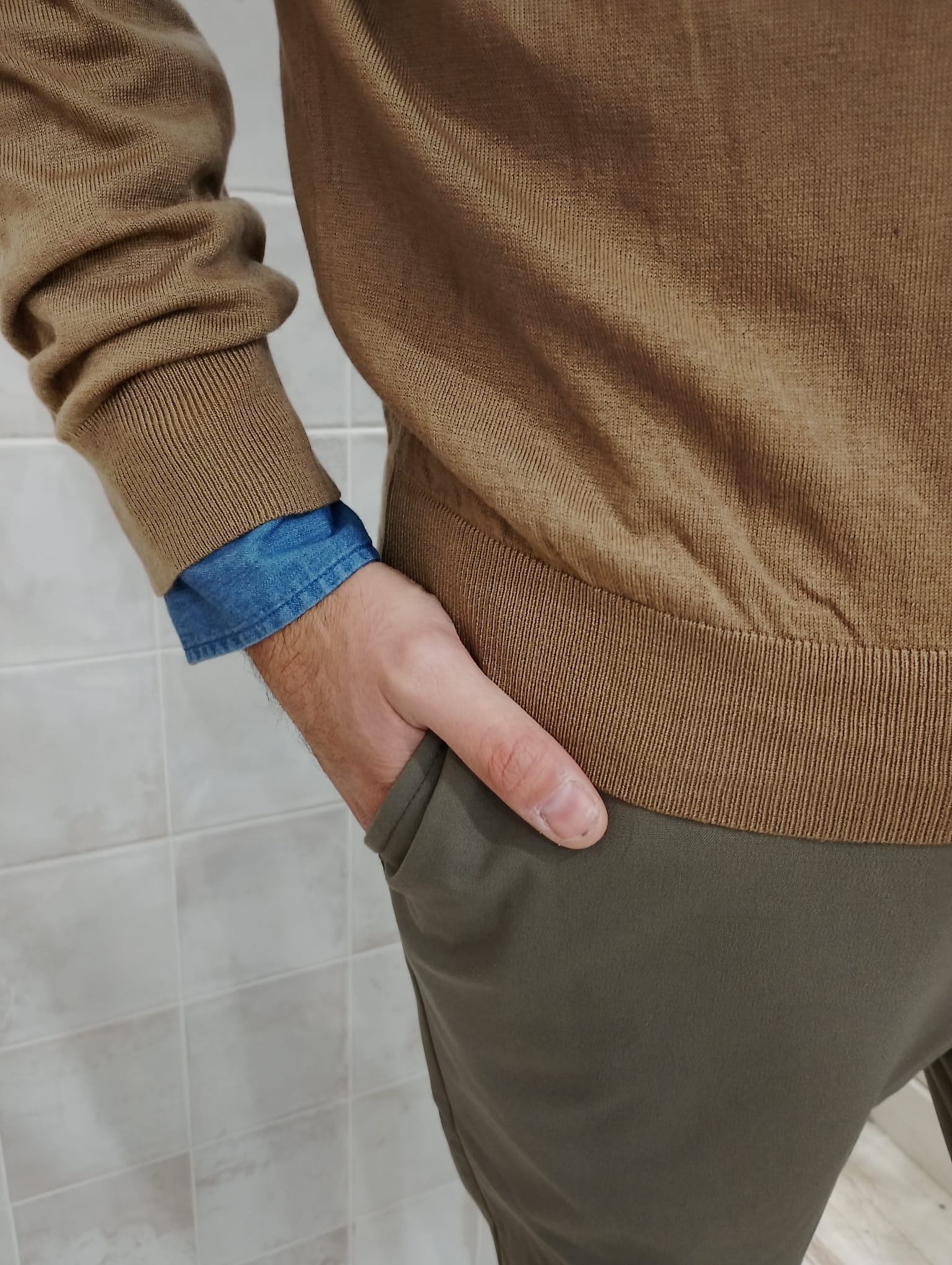 Detalle del puño del jersey color tierra de ORIGEN STUDIO y mano en el bolsillo del pantalón.