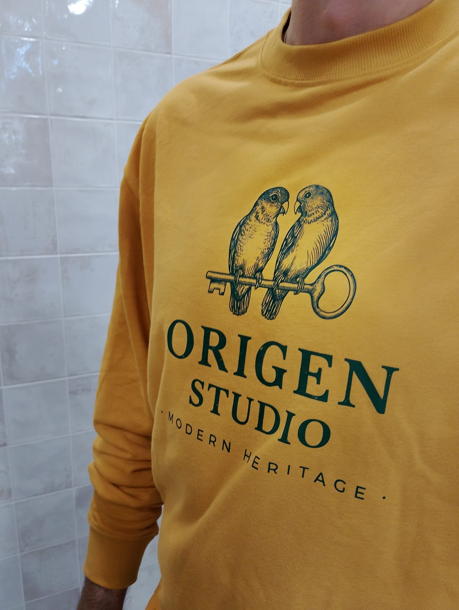 Primer plano del diseño Heritage Birds sobre sudadera color mostaza de Origen Studio