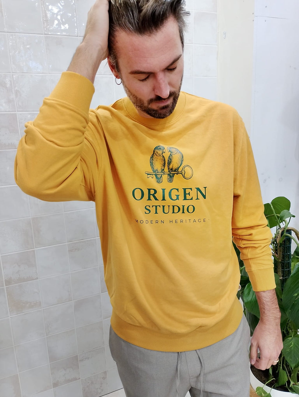 Sudadera Origen Studio Heritage Birds mostaza, vista frontal con modelo peinando el cabello